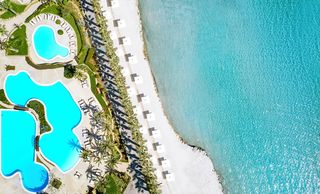 An Aerial shot of Sani Resort showing some of the pools at Sani Asterias and a section of beach with white sun loungers and parasols