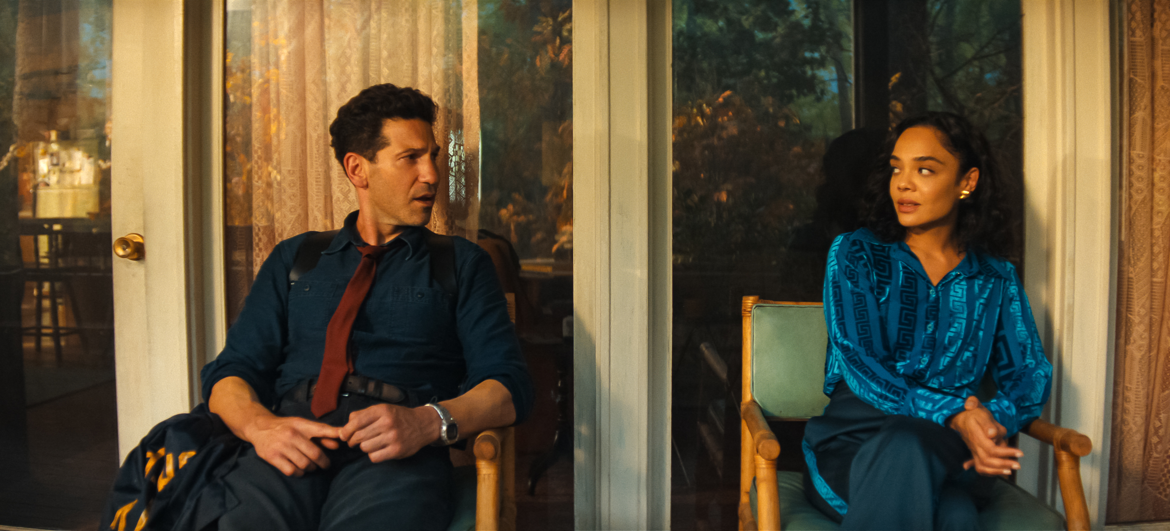 Jon Bernthal as Detective Jack Harper wearing a red tie and button down and Tessa Thompson as Anna wearing a blue top sitting on chairs on a front porch in Episode #101 of His &amp;amp; Hers