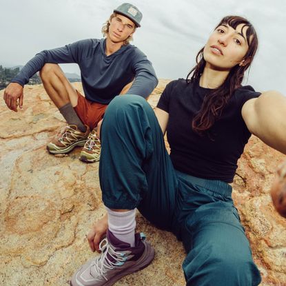 male and female models sat down wearing a black top and trousers, male is wearing a cap