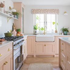 White painted kitchen with pink cabinets and a white ceramic sink with gold hardware