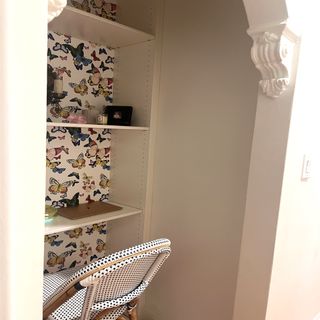 A cream built-in shelving unit with a laptop on the middle shelf, the bottom one removed to make space for a dotty black and white folding chair