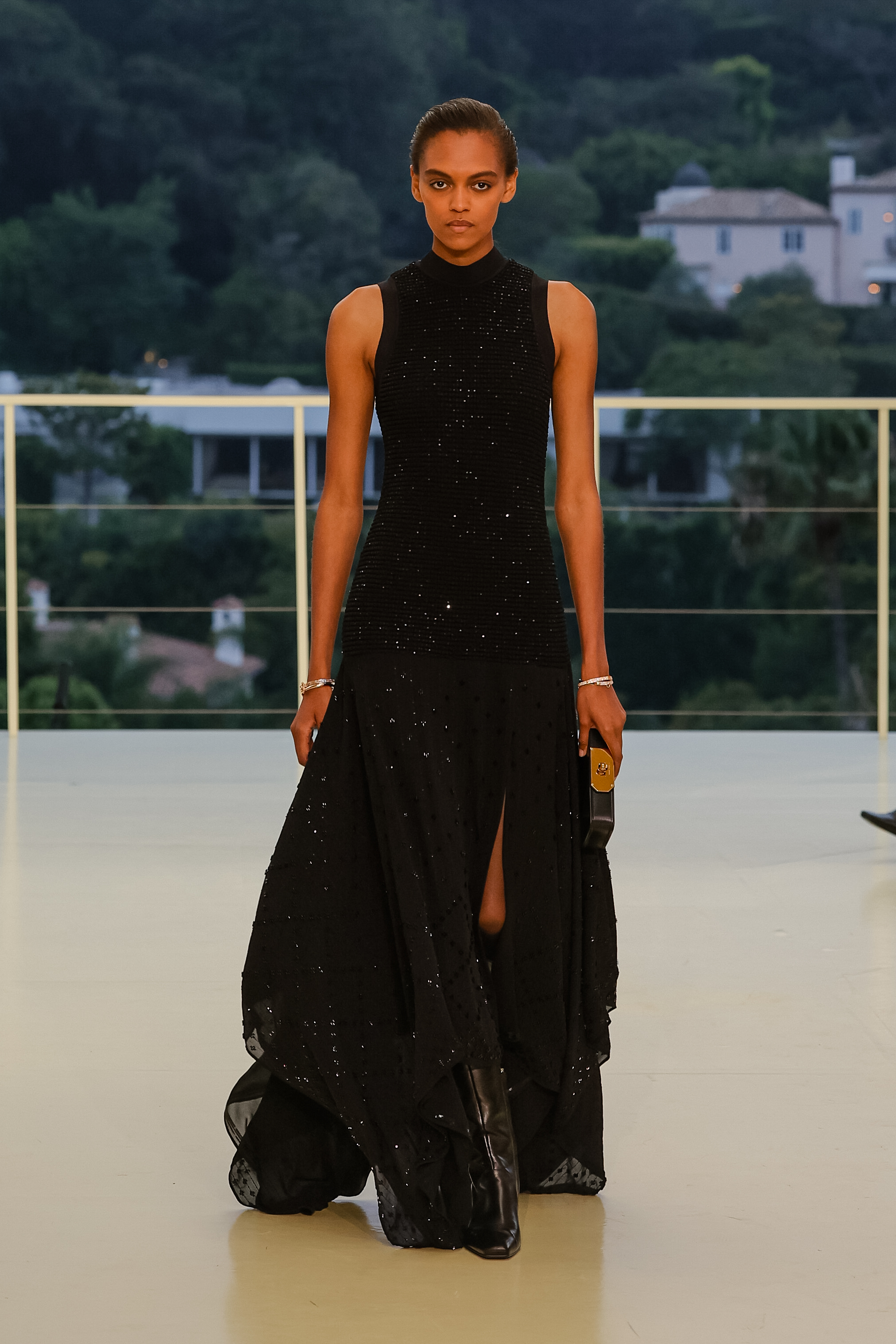 a woman wears a long black maxi dress with knee-high boots.