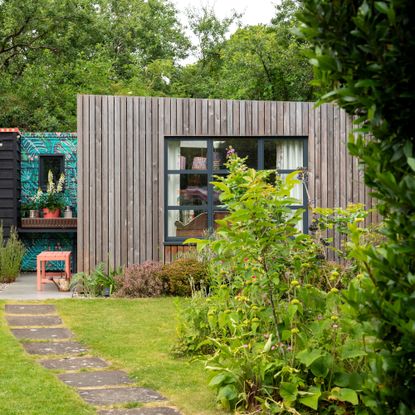 garden studio with vertical strip wood cladding and a hand-painted section of fence beside it