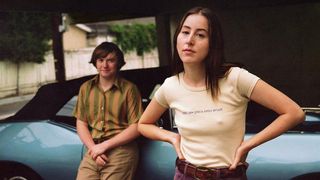 A still from the movie Licorice Pizza showing the two main characters Alana and Gary leaning against a blue car.