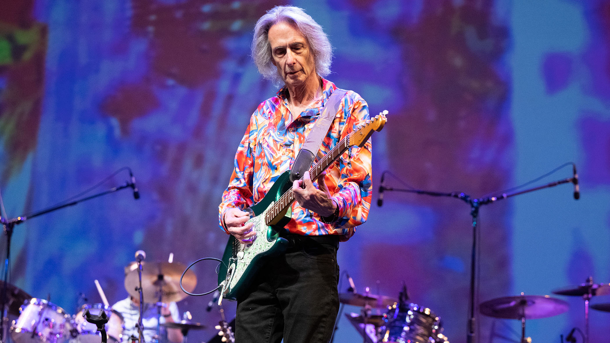 Lenny Kaye plays a green Strat and wears a brightly patterned shirt onstage.