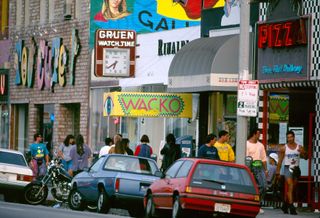 A street shows colorful, art deco signs and plenty of walkers passing by.