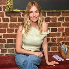 Sienna Miller is photographed wearing jeans with white bow heels and a sage off-the-shoulder top.