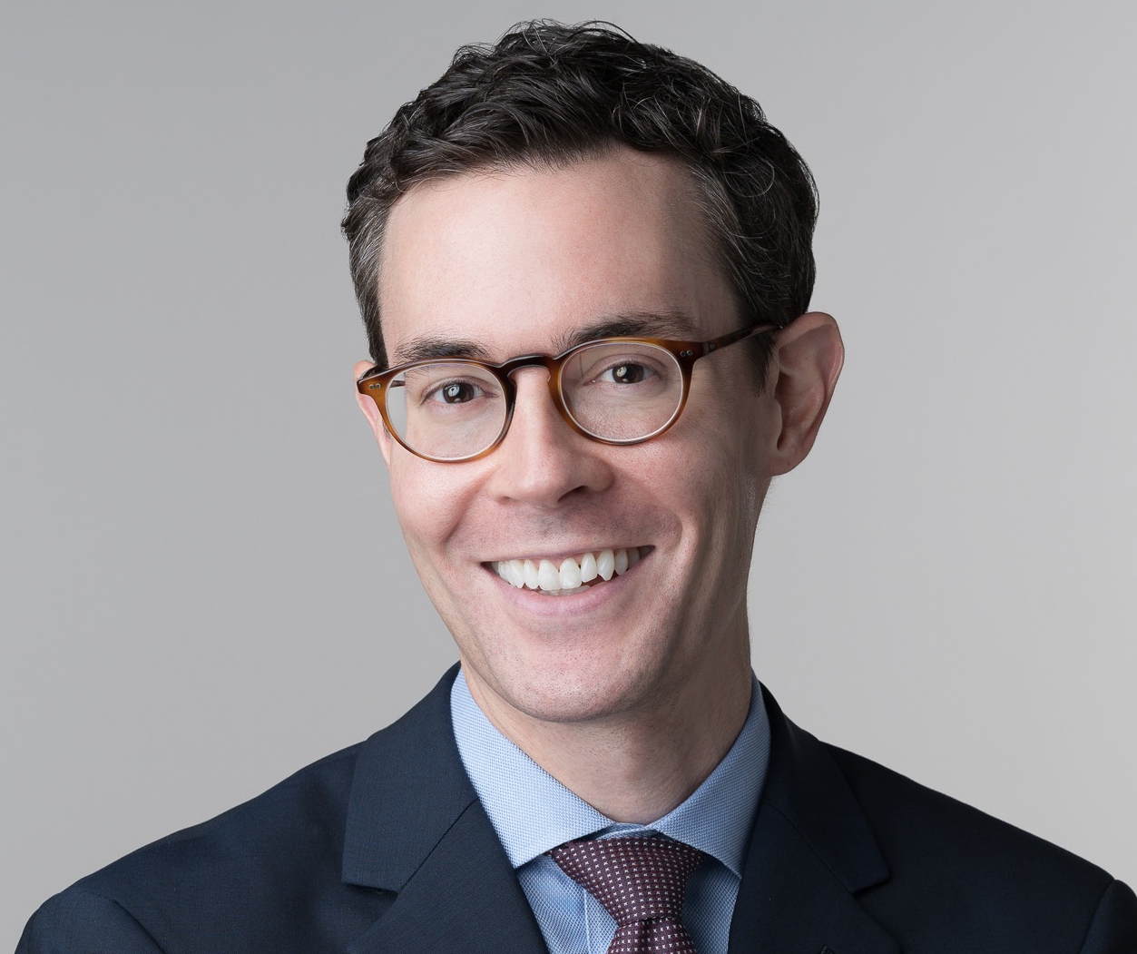 a white man with short brown hair and glasses wearing a jacket and tie