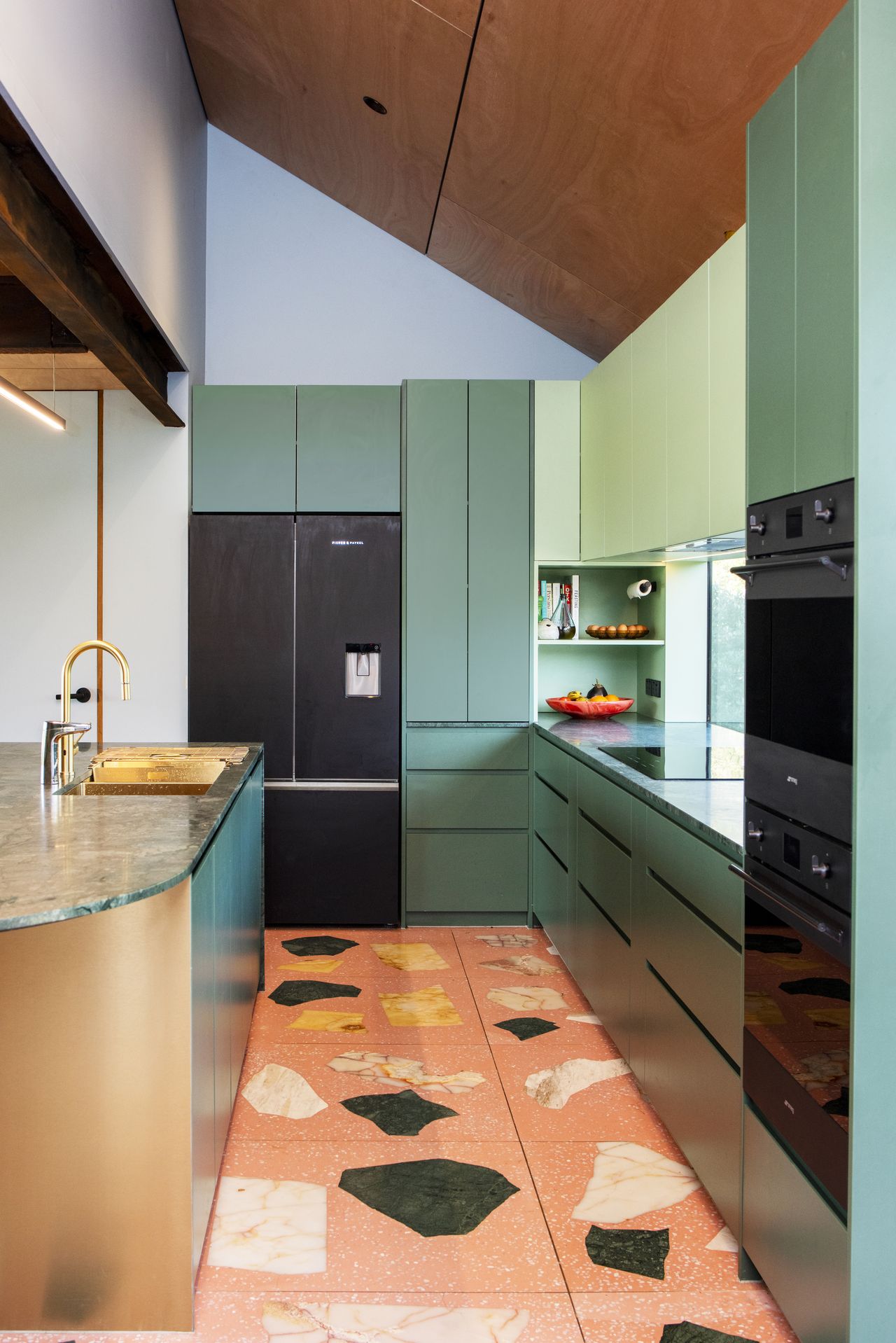 colorful kitchen with orange stone floor, green cabinets, bronze island, light blue walls, and timber ceiling