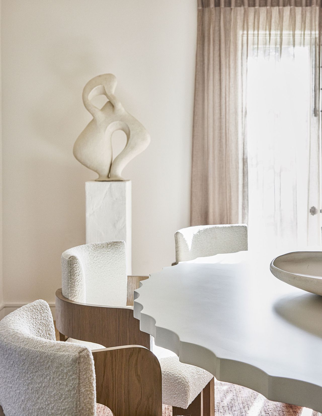 A close up of white boucle chairs with wooden frames and a curved edge table in a white neutral room
