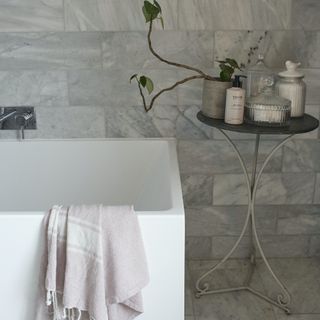 white bath, marble tiles and table laden with toiletries