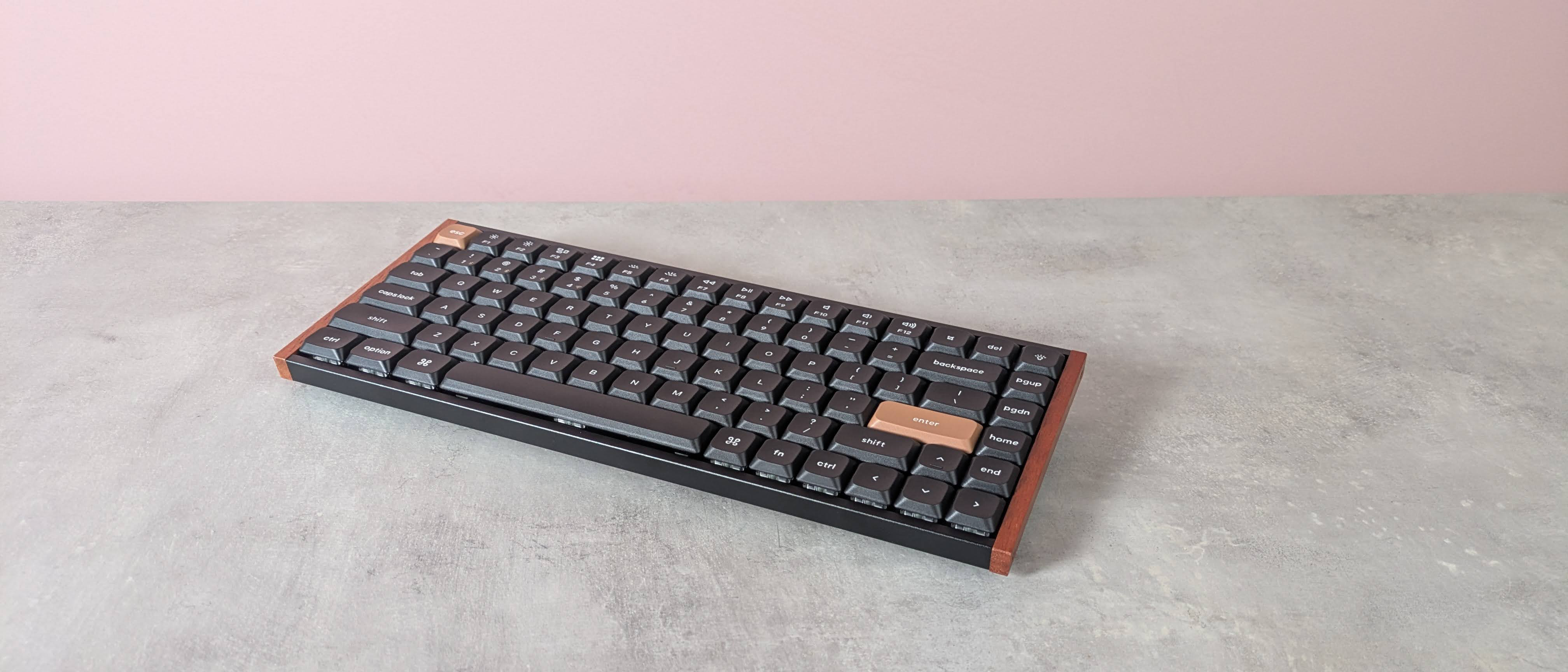Three-quarter view of Keychron K3 HE on a desk with pink wall in background