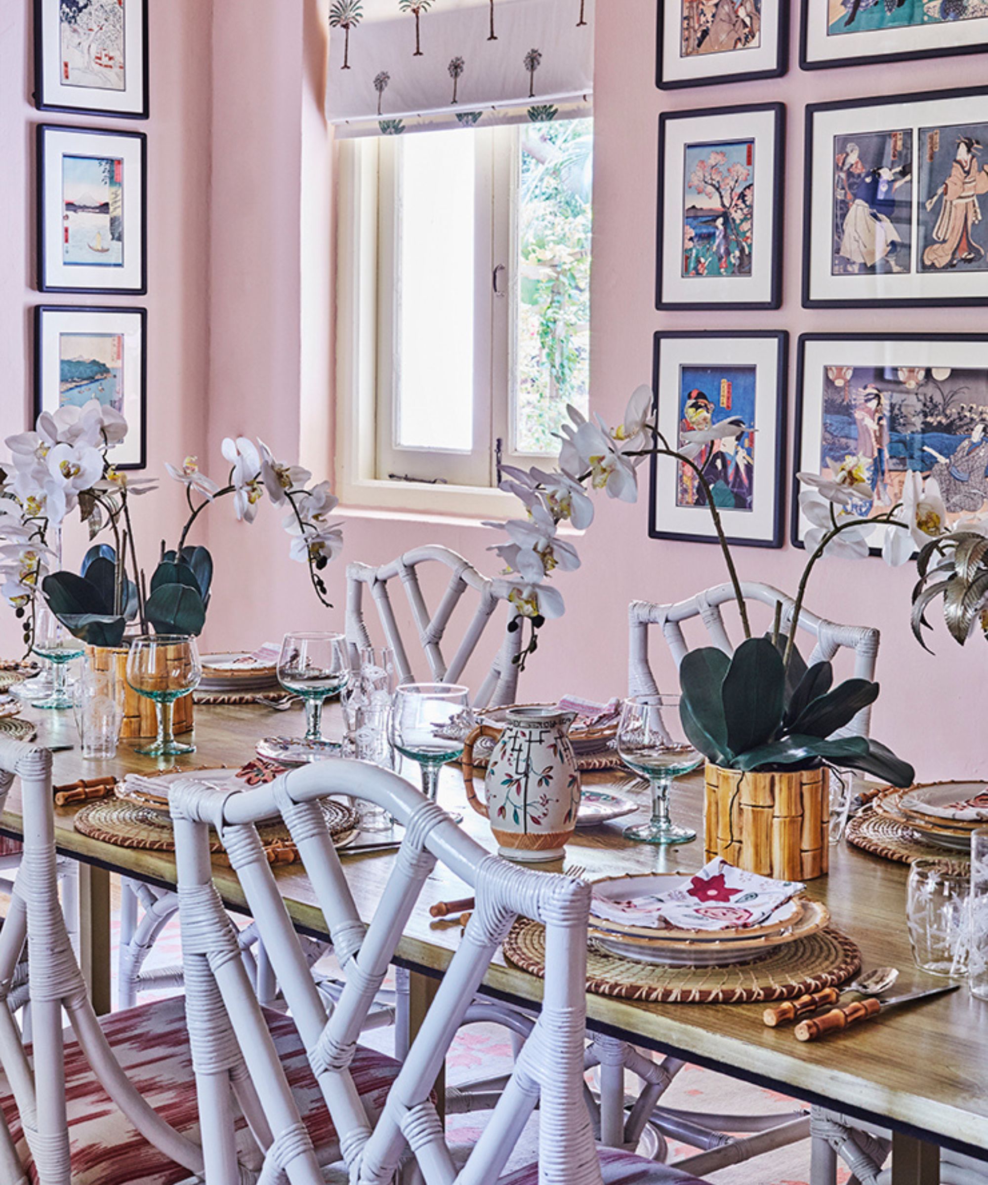Pink dining room with white wicker chairs, wooden table, and rattan charger plates