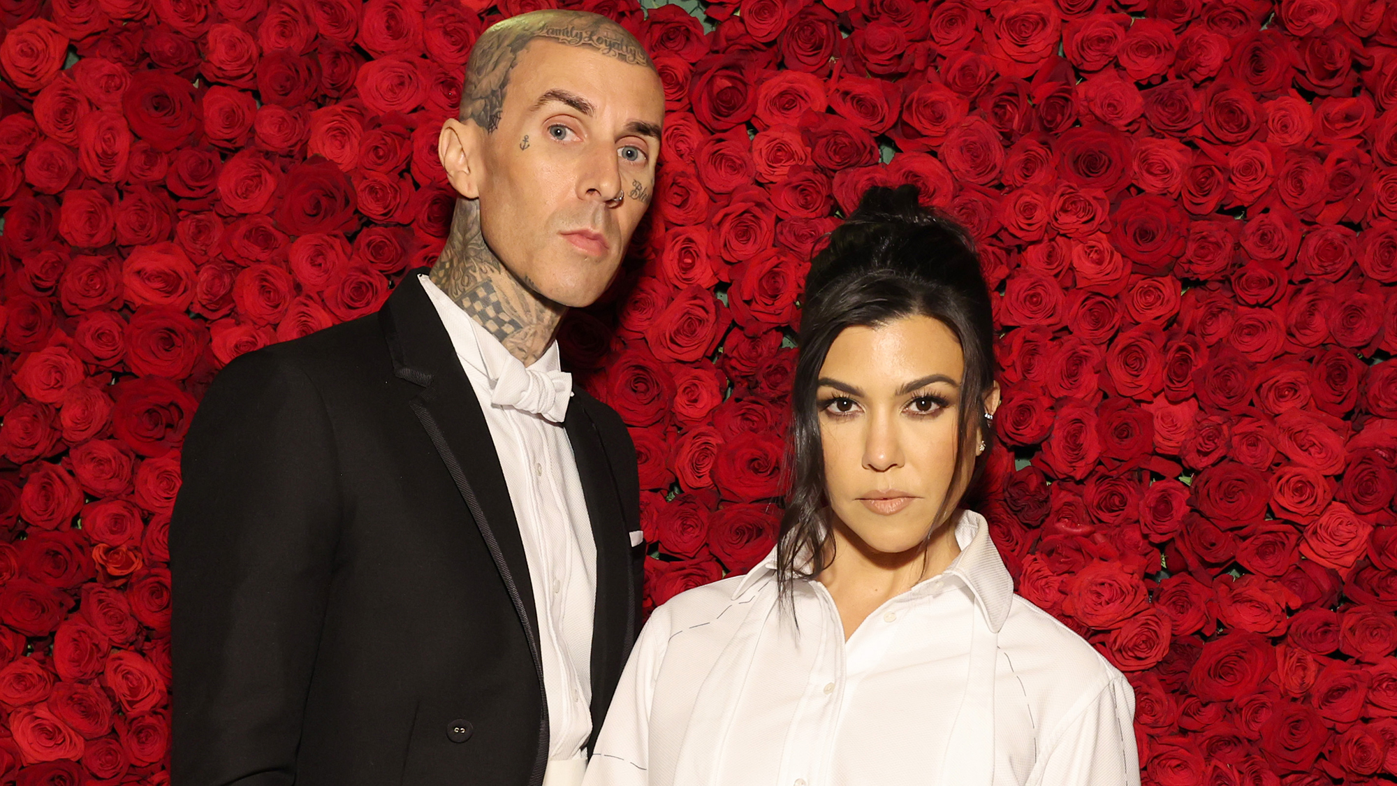 Travis Barker and Kourtney Kardashian in front of a red roses background at The Met Gala