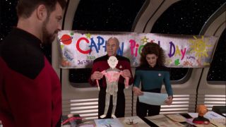 three people in starfleet uniforms look at children's decorations inside a futuristic spaceship