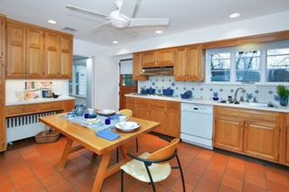 A kitchen with wooden cabinets, and terracotta floor tiles