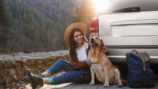 girl sitting by her car with one of the best dog breeds for travel