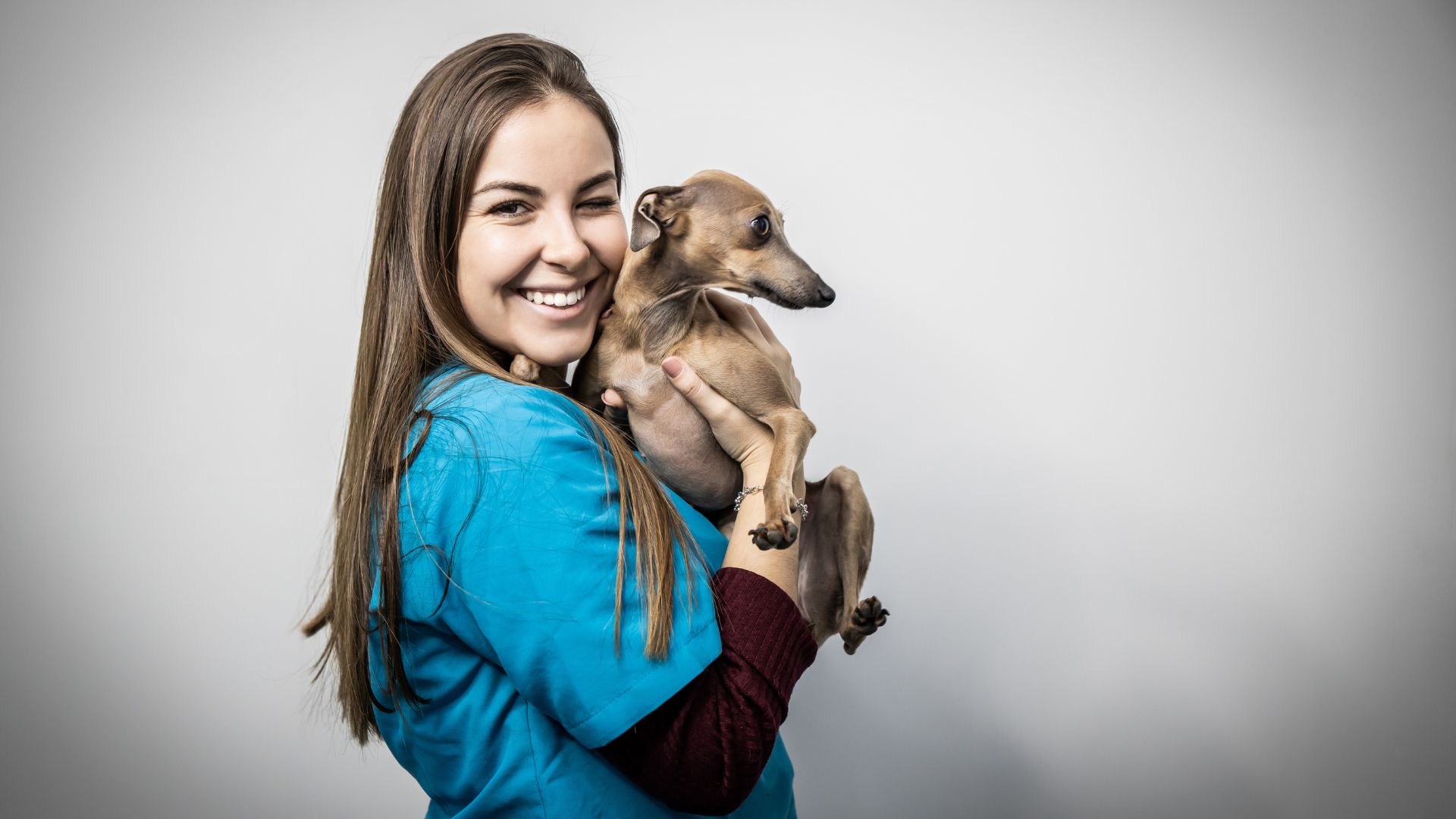 Things vets wish they could tell pet owners: woman vet wearing blue overall smiling and hugging dog