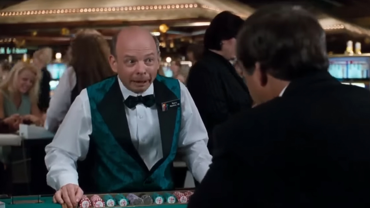 Wallace Shawn dressed as a casino dealer making fun of Chevy Chase