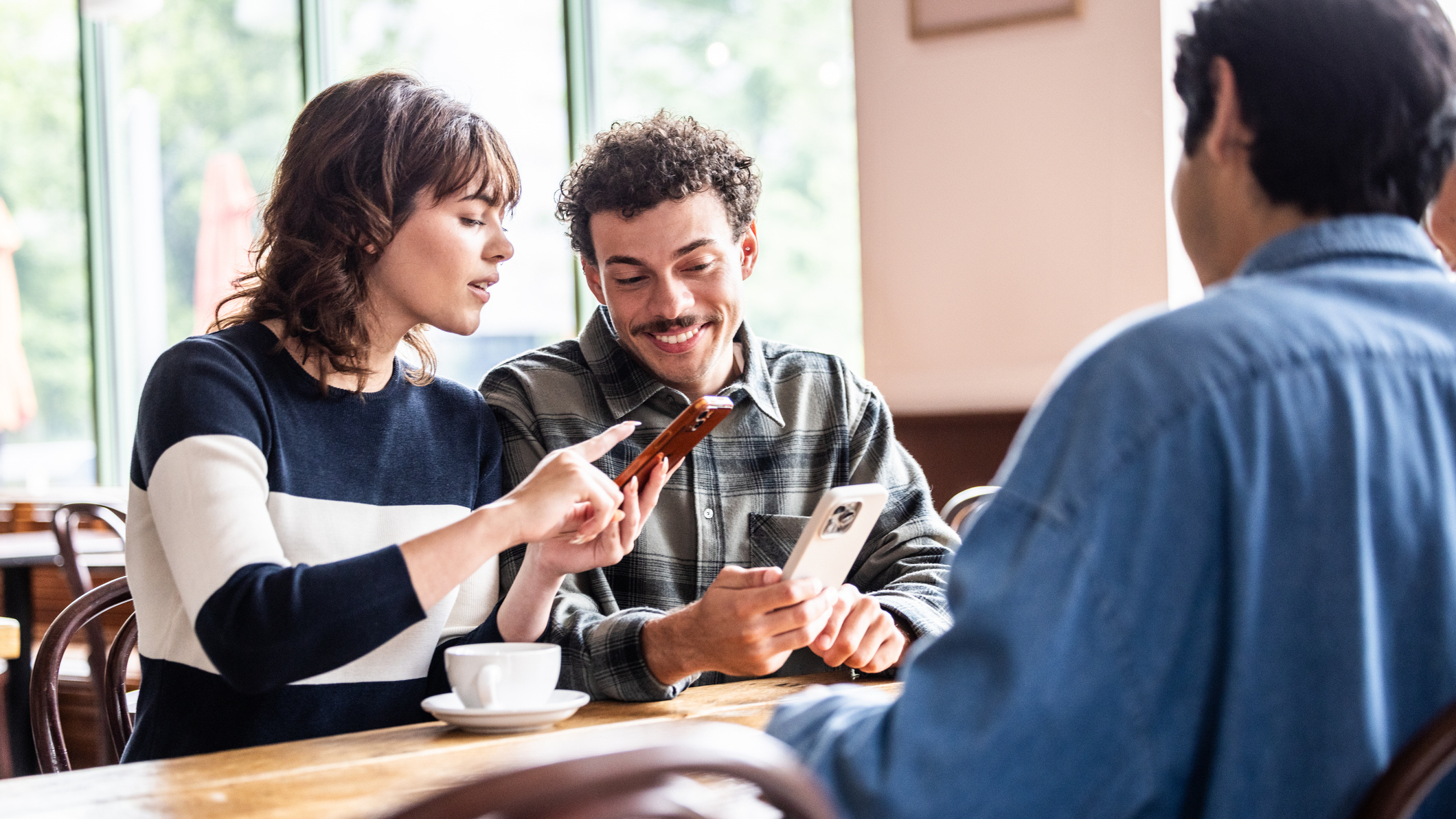 People sat around table having coffee, looking at their phones