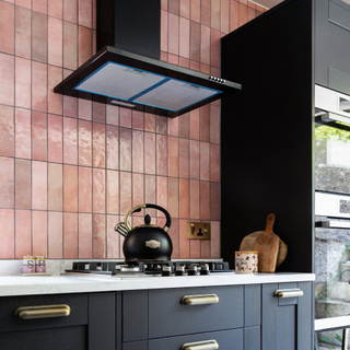 Black Kitchen worktops with pink tiling. There is a matte black kettle on top of the stove