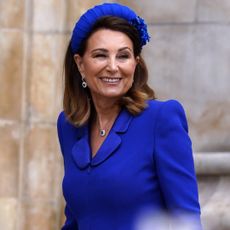 Carole Middleton wears a royal blue outfit and matching hat, while Kate Middleton waves on a beach