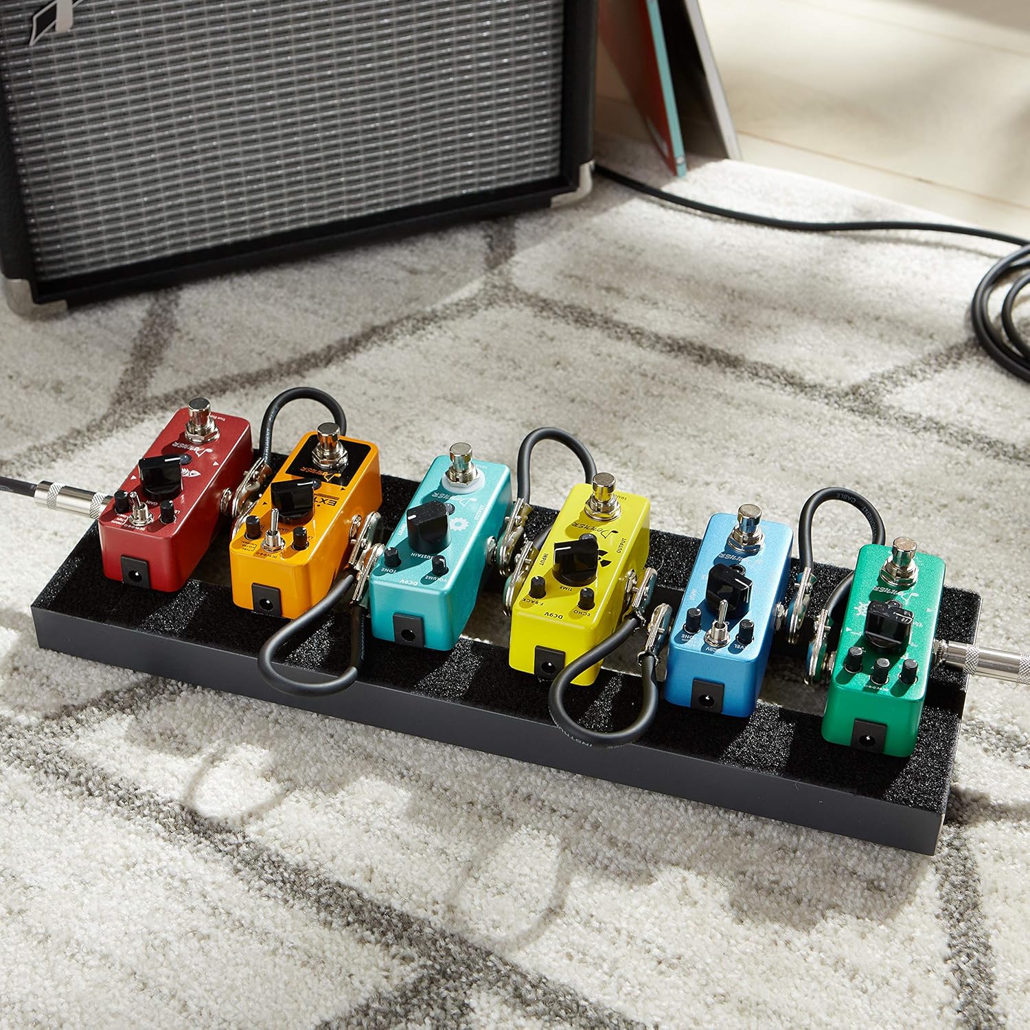 Micro pedals on a small pedalboard, connected with patch cables, and an amp in the background