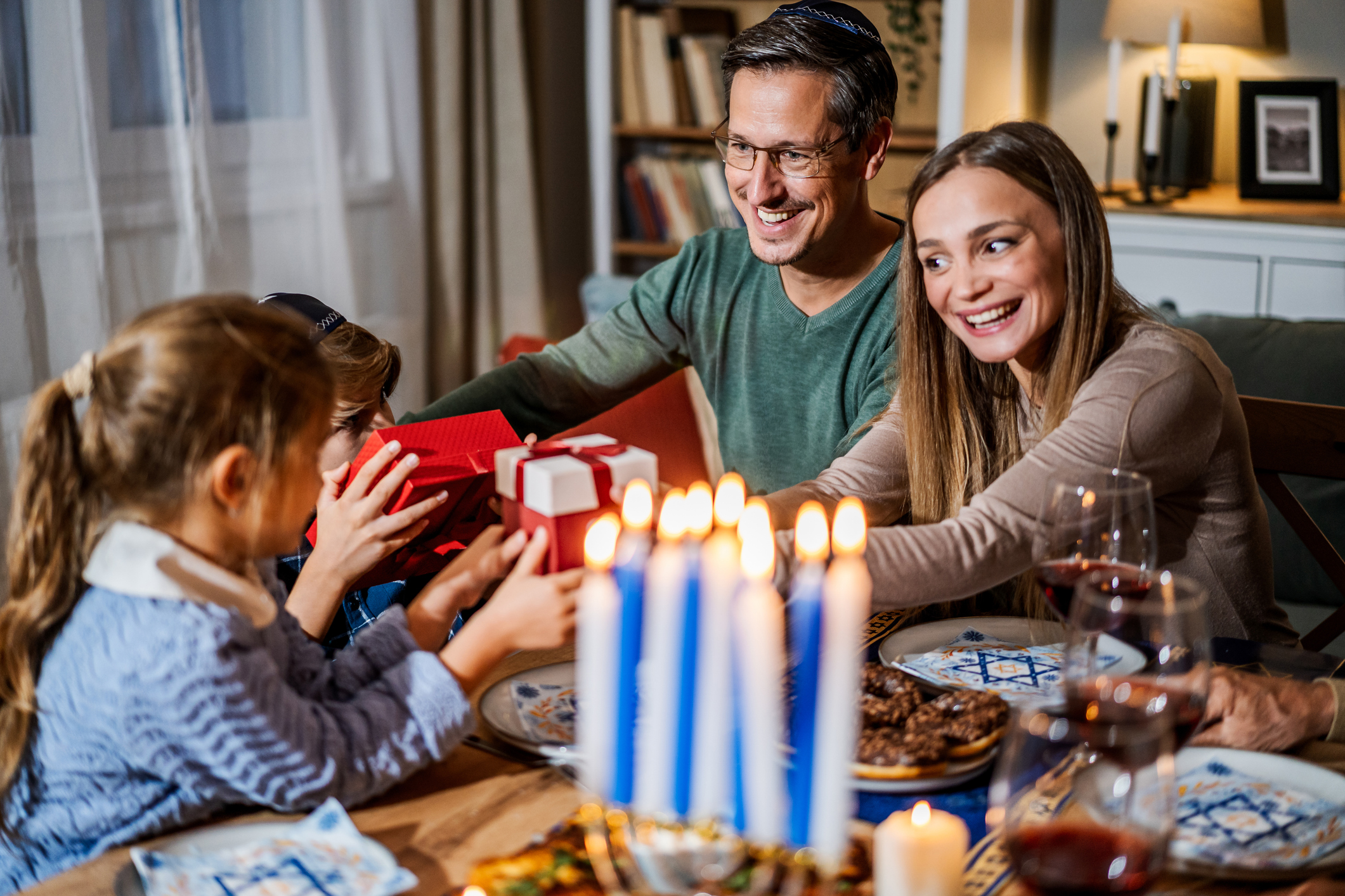 A young couple celebrating Hannukah with a kid passing gifts.