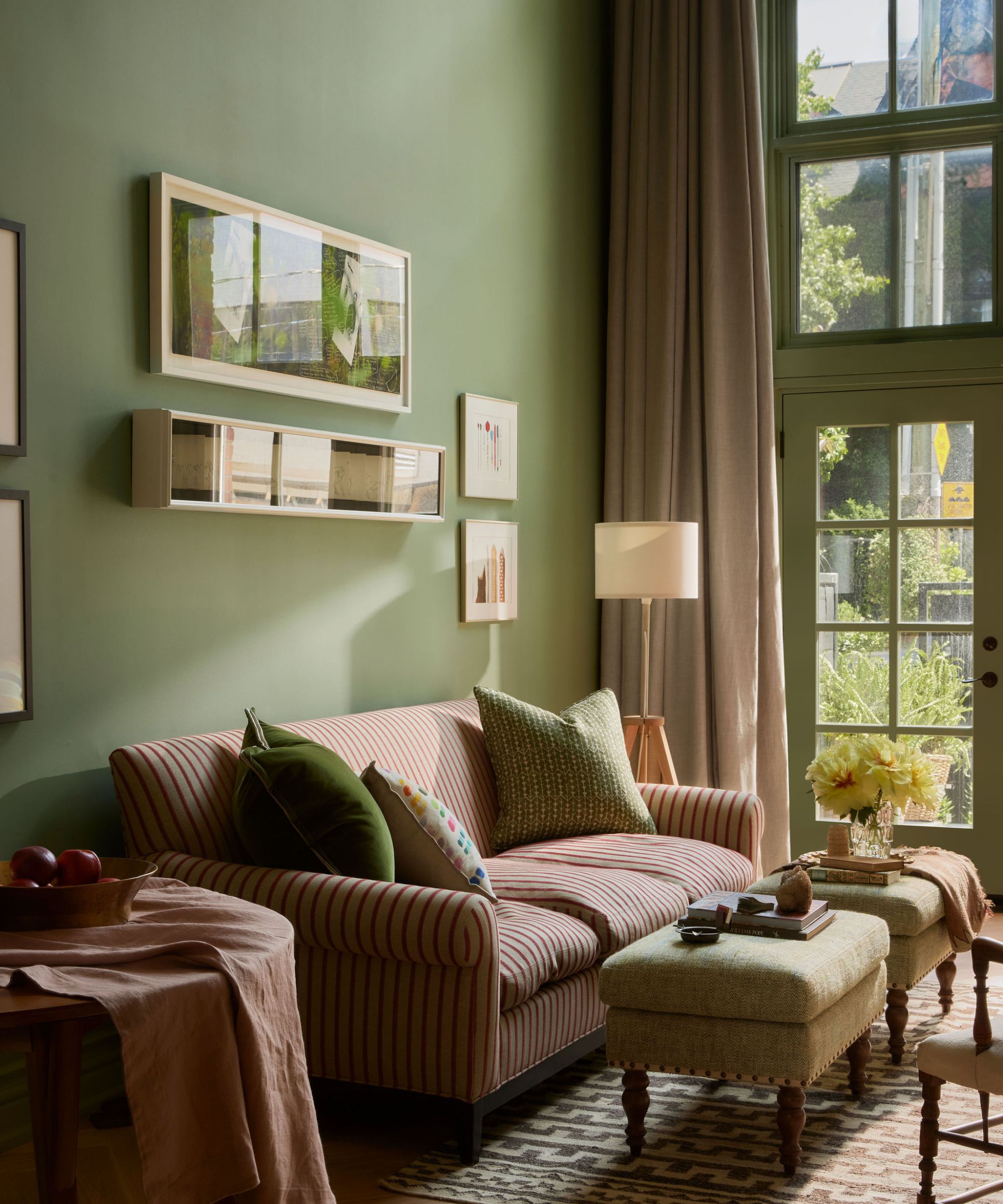 A cozy living area with green walls, a striped sofa, a pink armchair, and large glass doors opening to a patio