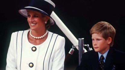 Princess Diana wears a white blazer with navy blue piping and buttons with a matching hat as she sits with a young Prince Harry in a suit