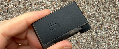 Holding the iFi GO Blu Air in a hand, with a pebbledashed wall behind it