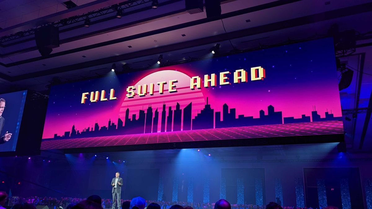 A wide-angle shot of NetSuite EVP Gary Wiessinger, giving a keynote speech with a large screen above displaying &amp;quot;FULL SUITE AHEAD&amp;quot; in retro arcade letters