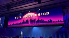 A wide-angle shot of NetSuite EVP Gary Wiessinger, giving a keynote speech with a large screen above displaying "FULL SUITE AHEAD" in retro arcade letters