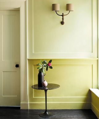 Painted hallway in two different shades of yellow, black wooden flooring, twin wall lamp, black side table