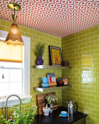 Green metro tiles in kitchen corner with open shelving, cute accessories and pink patterned wallpapered ceiling