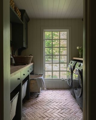 House Seven Design Laudry Room with dark cabinetry. terracotta floor and laundry carts under countertop