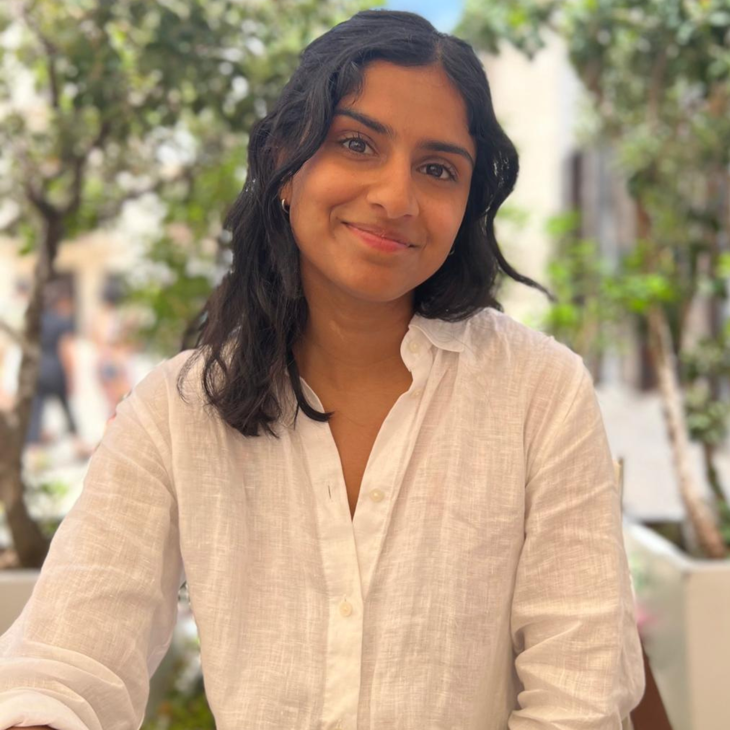 A woman with black wavy hair in a white linen button down