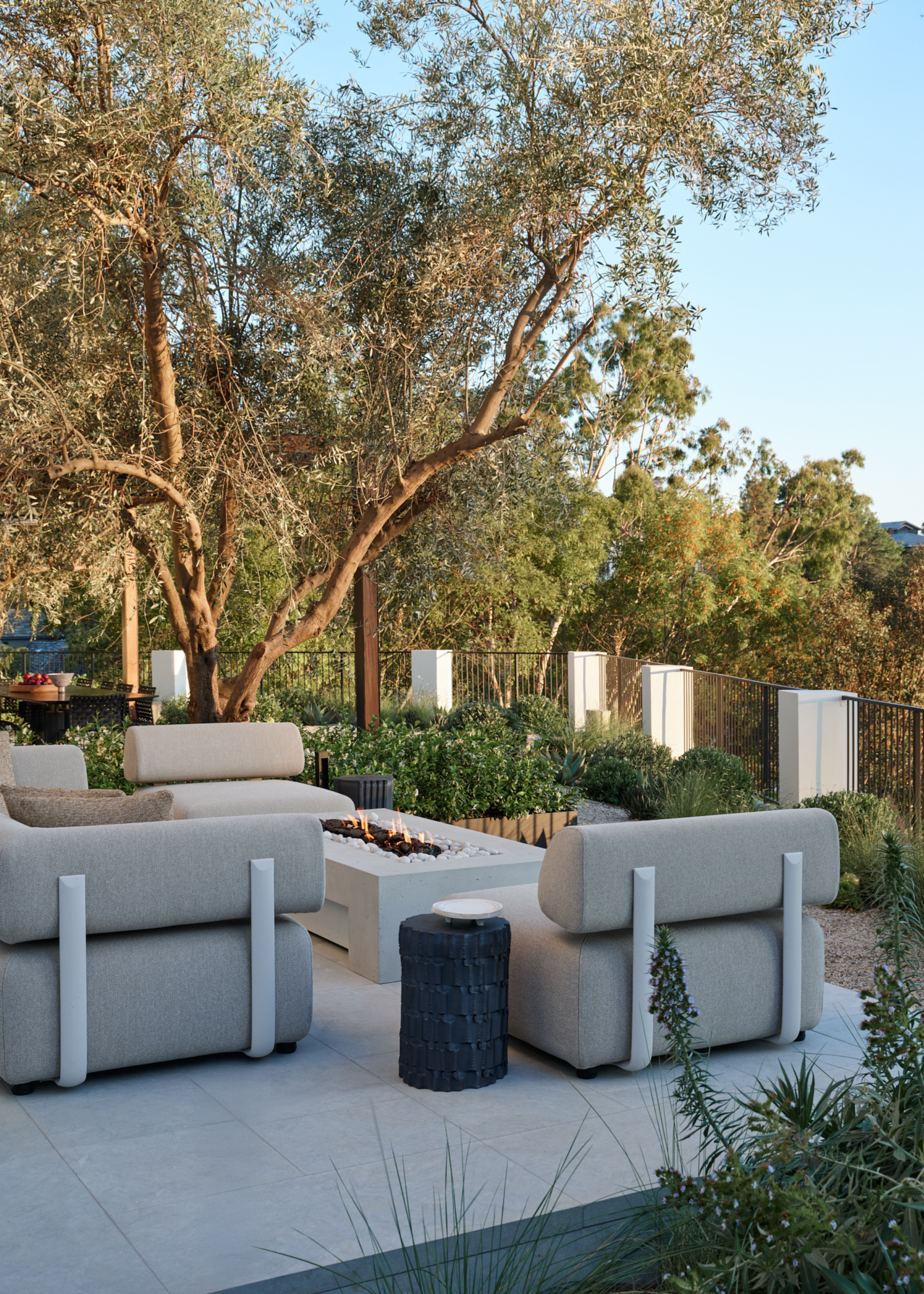 An outdoor living room with gray sofa chairs and a white firepit table alongside a black side table