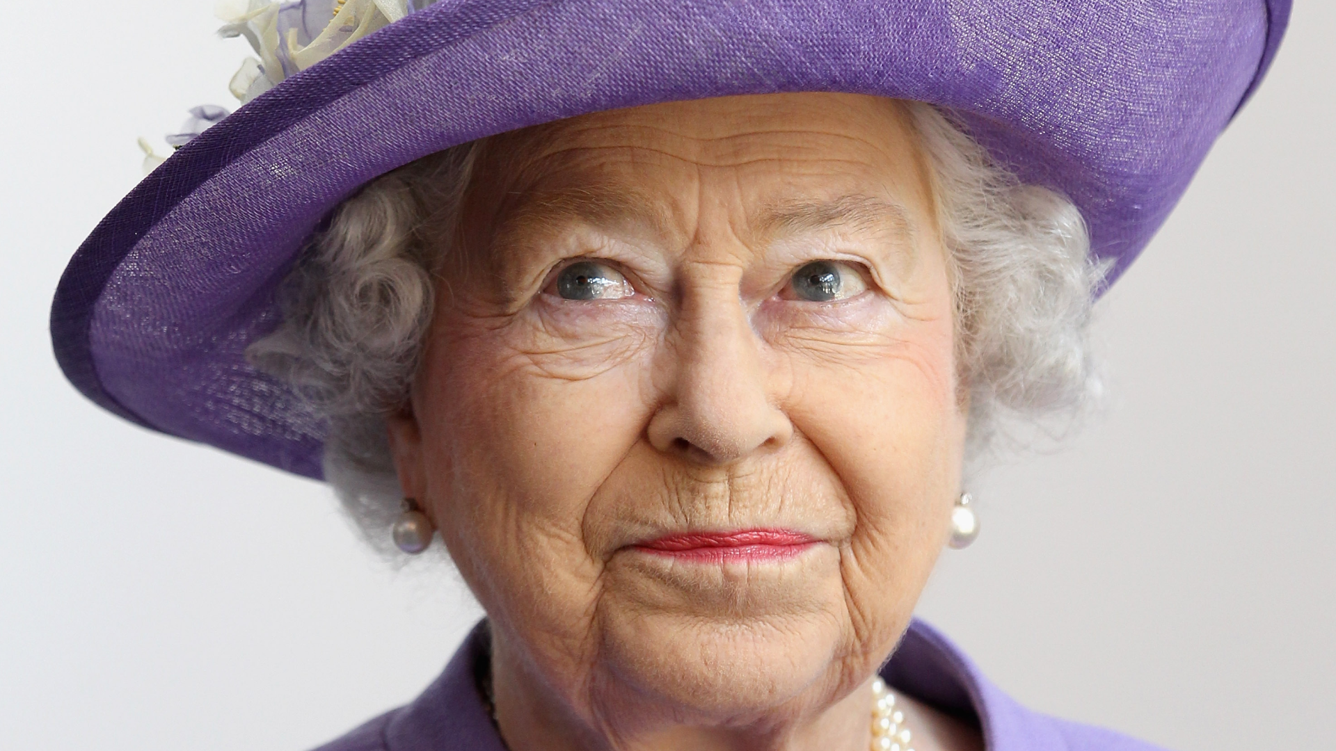Queen Elizabeth wearing a purple hat and smirking
