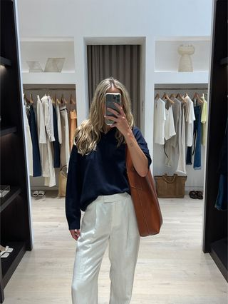 Eliza Huber in the dressing room at Banana Republic wearing a navy blue cashmere sweater with white linen pants and a brown leather bag.