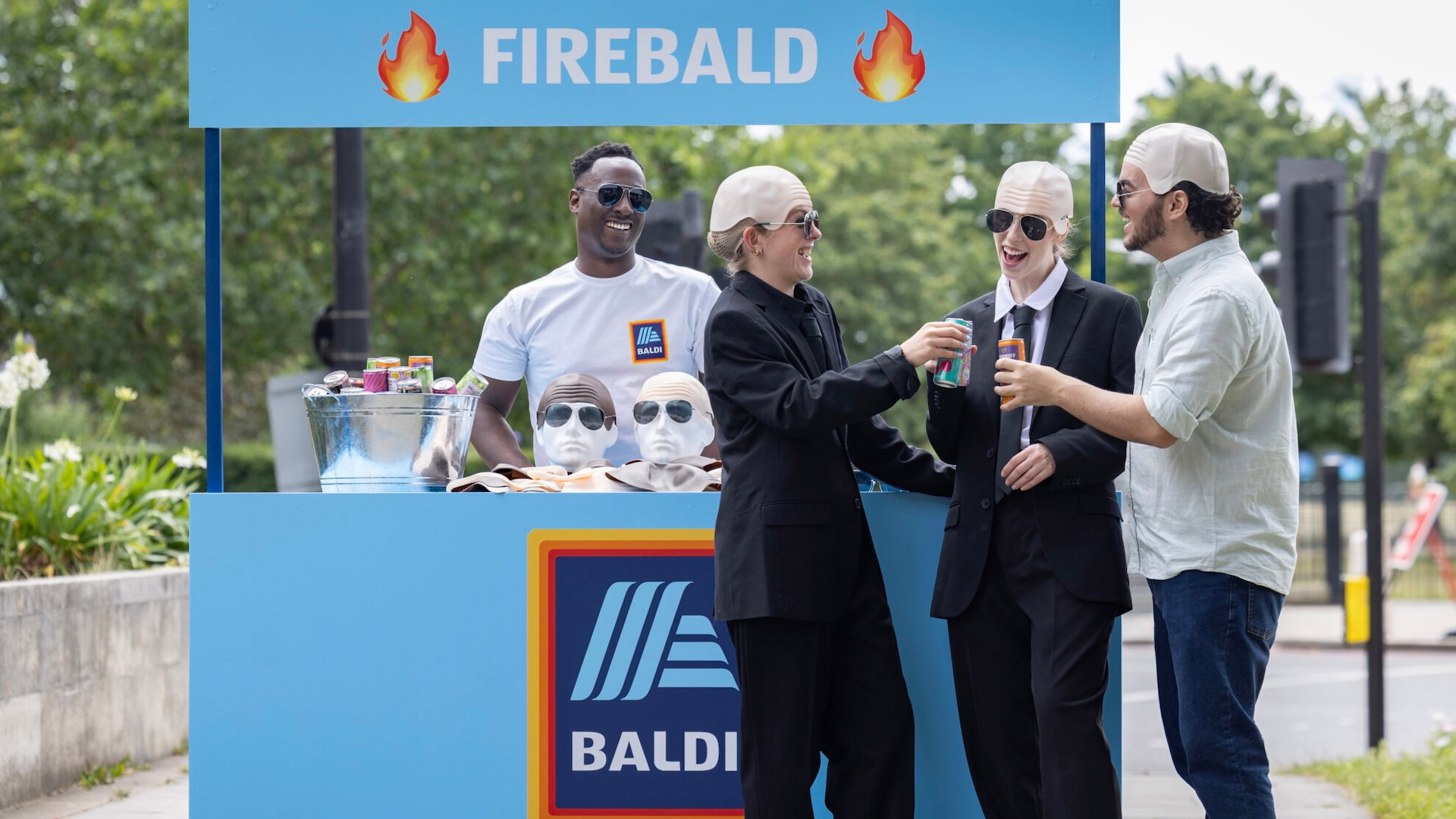 Two people standing in front of a stand with bald caps on 