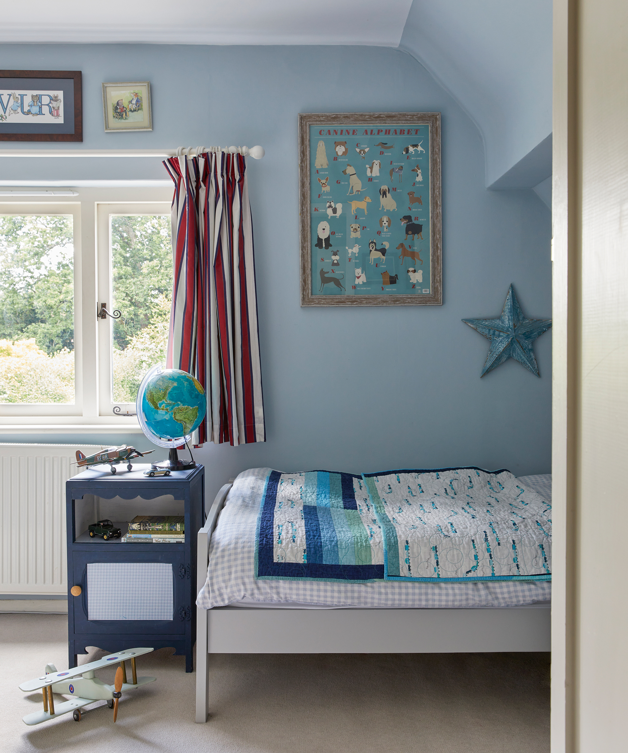 boy's bedroom with light blue walls, white and red striped curtains and patchwork bedspread