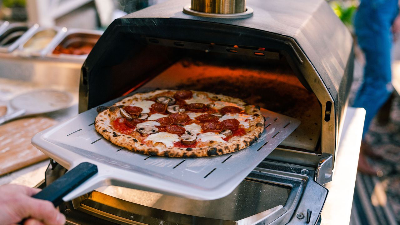 person cooking pizza in a tabletop pizza oven