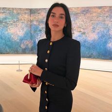 Dua wears a buttoned long-sleeve dress and red clutch.
