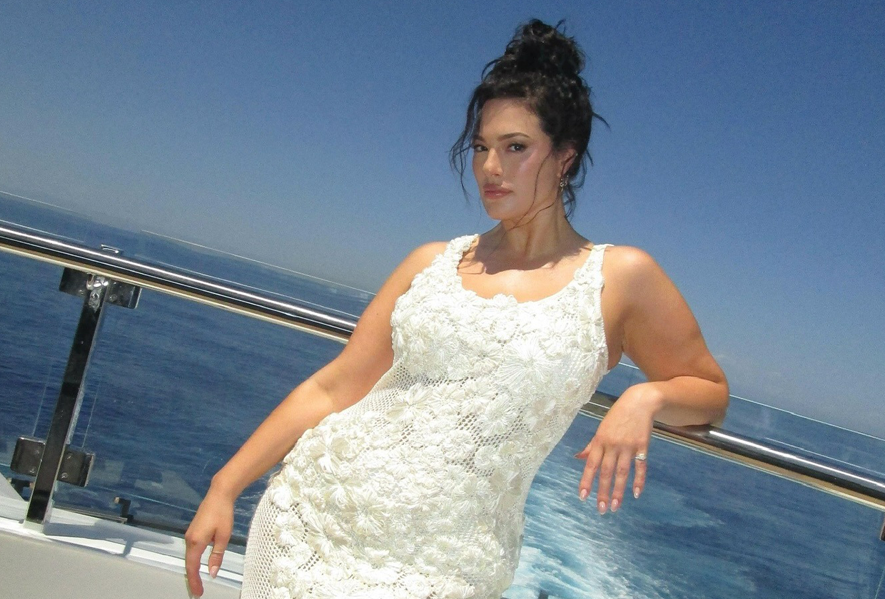 Ashley Graham wearing white floral embroidered maxi dress while standing on yacht.