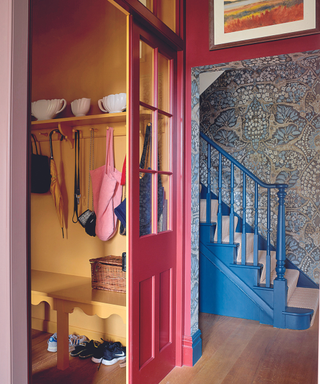 Hallway with staircase painted in blue with patterned wallpaper and next to entrance to cloakroom painted in yellow visible through hallway painted in red