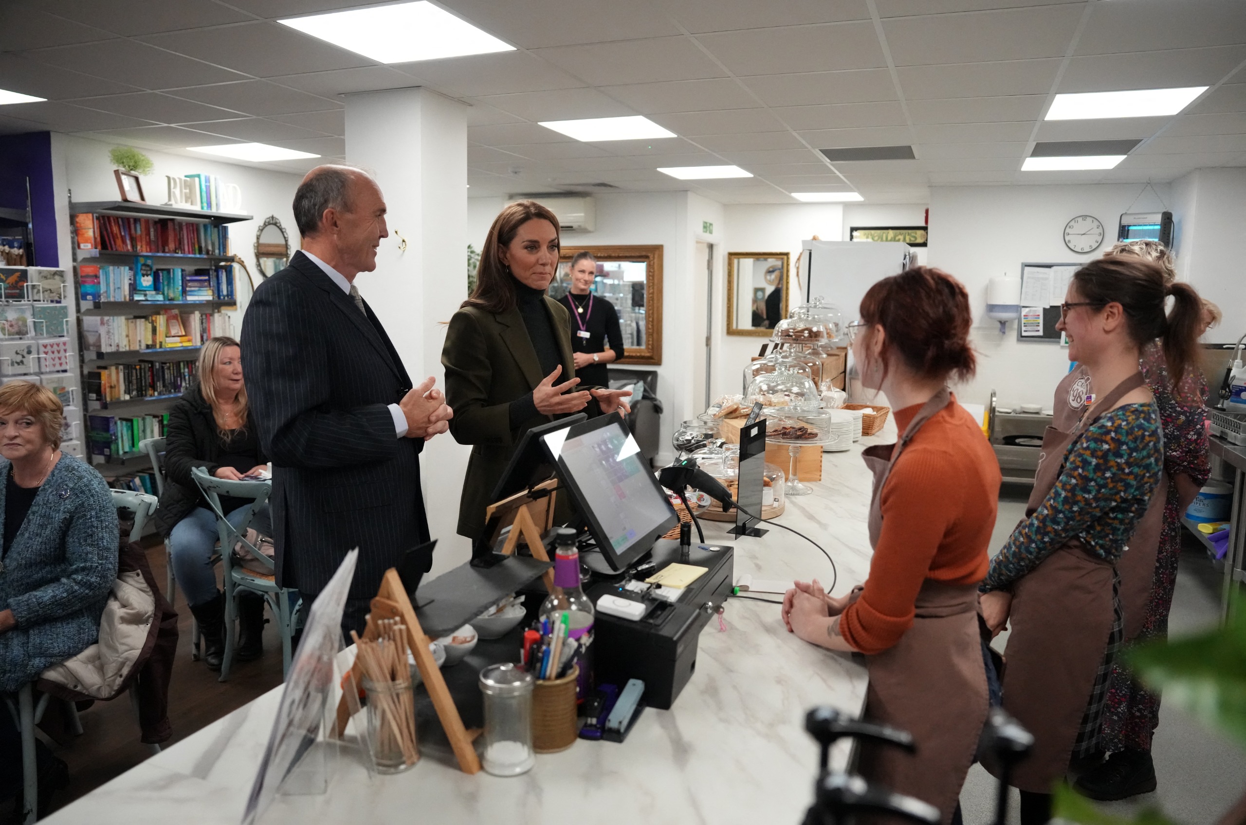 Princess Kate standing behind a counter talking to coffee shop workers