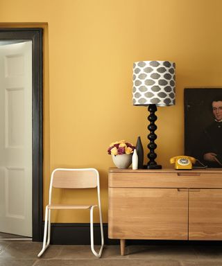 A yellow living room with a wooden sideboard next to a chair