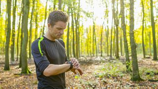 Runner checking GPS watch in woodland