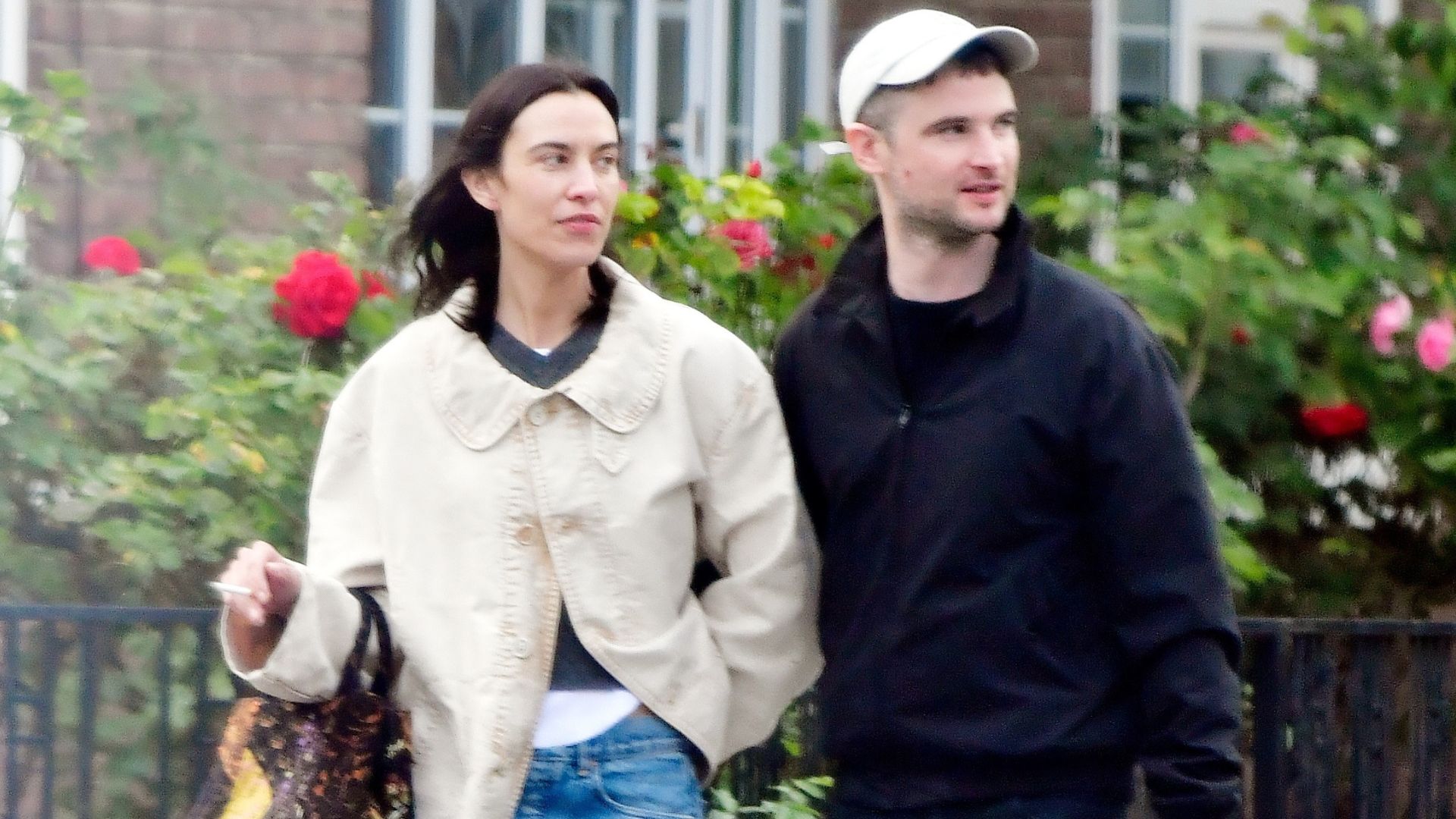 Alexa Chung walks down the street wearing blue jeans with black ballet pumps and a cream jacket.